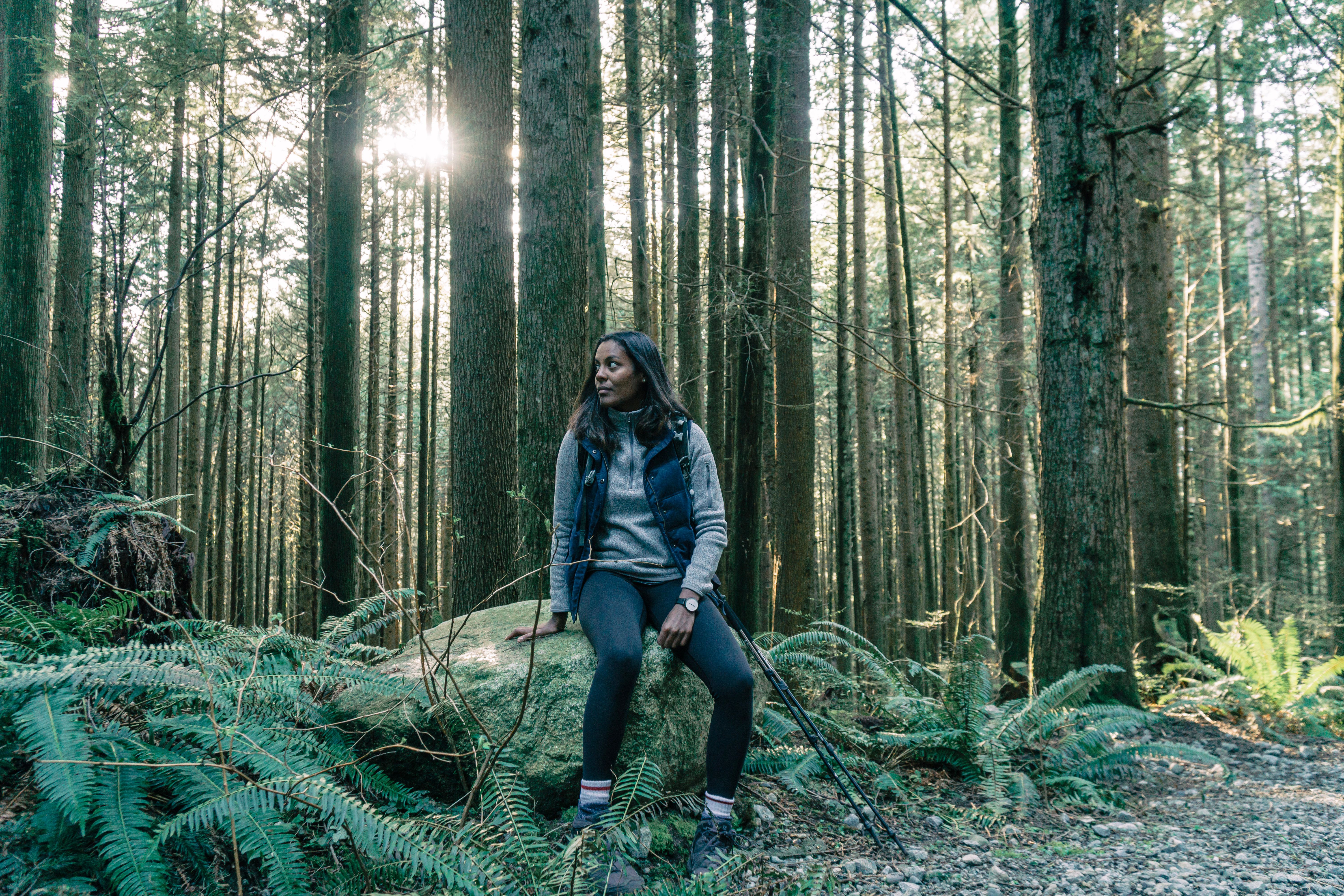 Woman resting on a boulder surrounded by forest trees during a hiking trip.