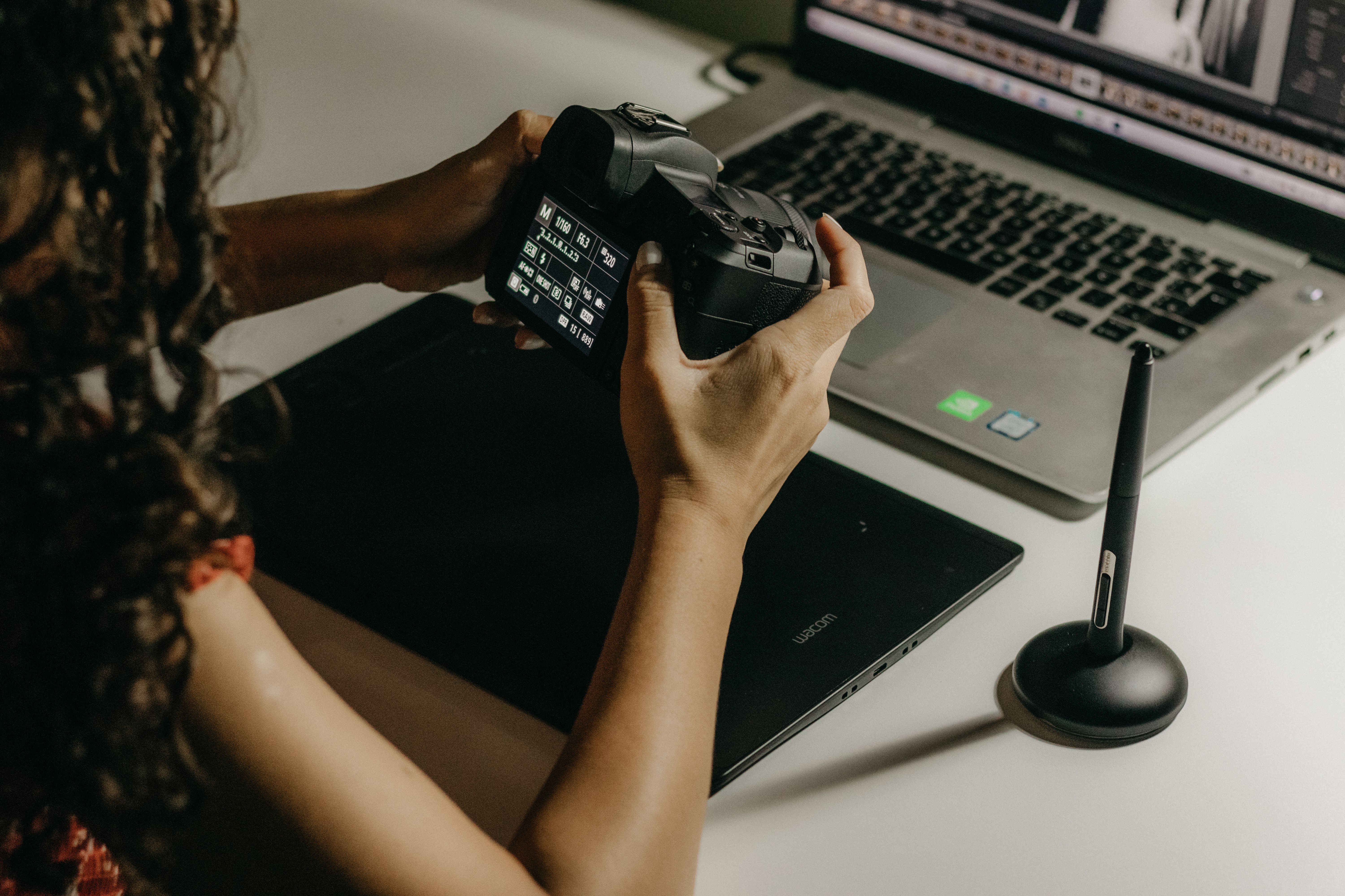 A woman reviews and edits her photos using a camera and laptop at a desk.