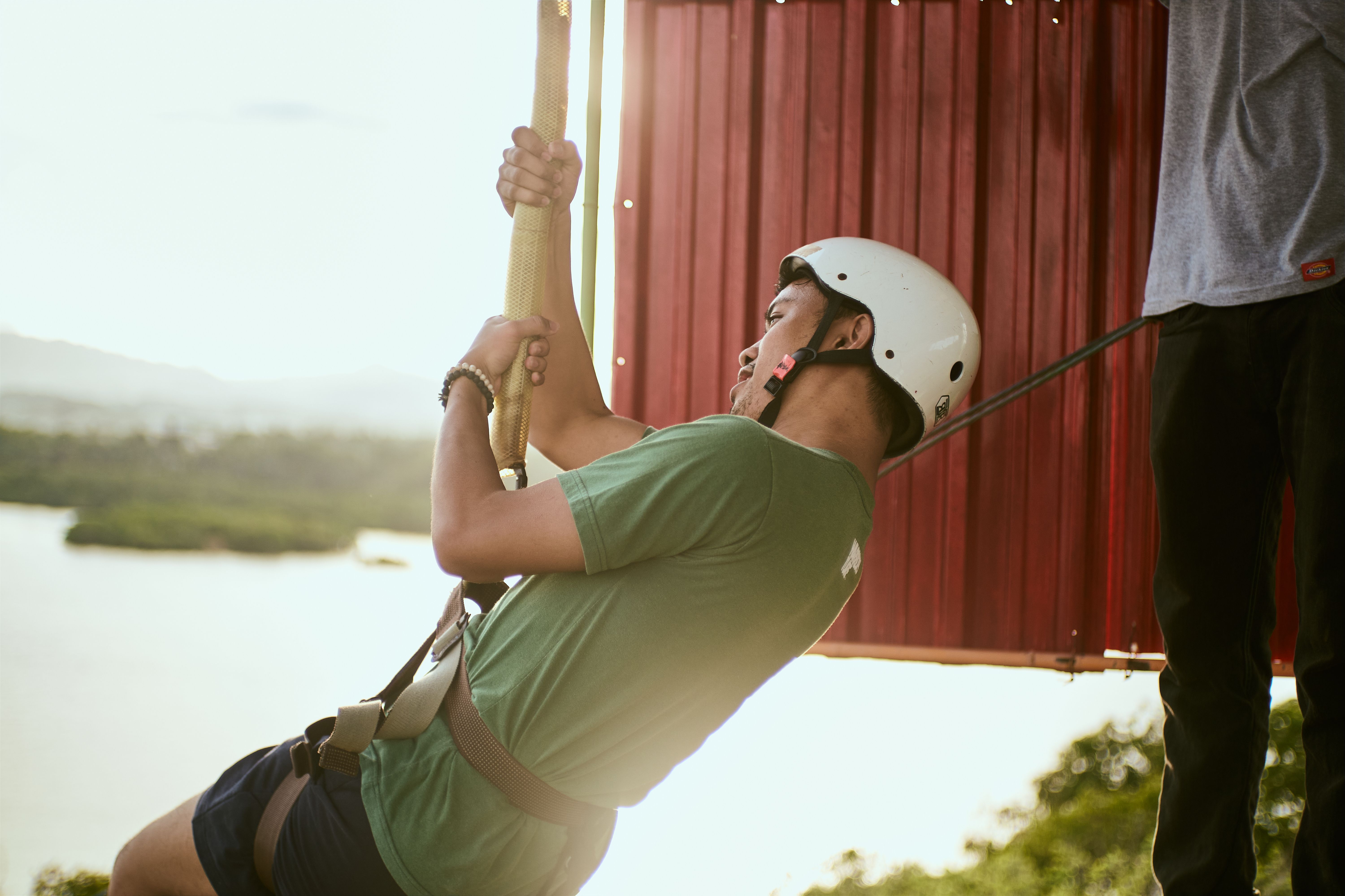 Man enjoying a thrilling zip line ride with a scenic background at sunset.