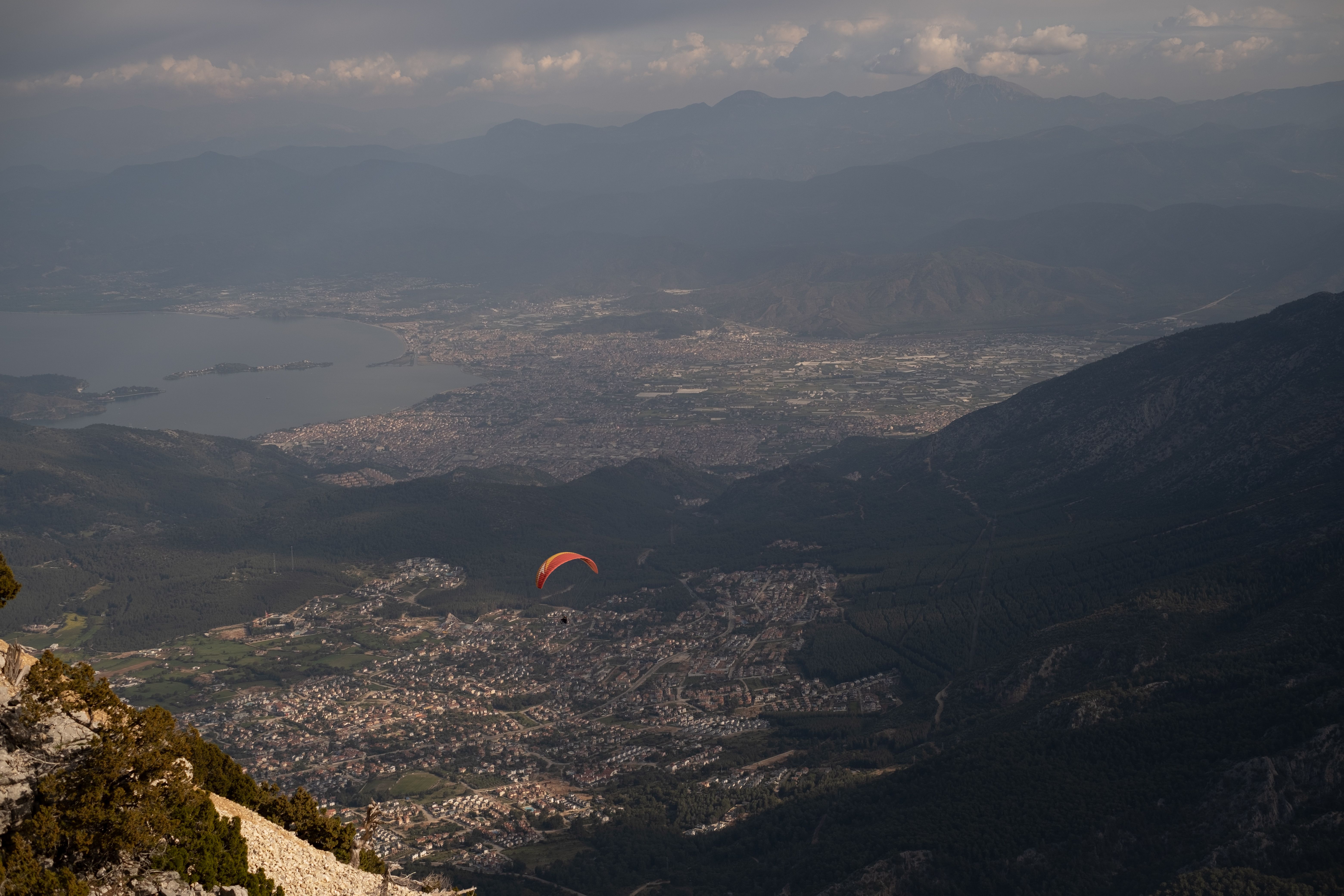 A scenic aerial view of a paraglider soaring over Babadağ Mountain in Turkey, capturing the expansive landscape and city