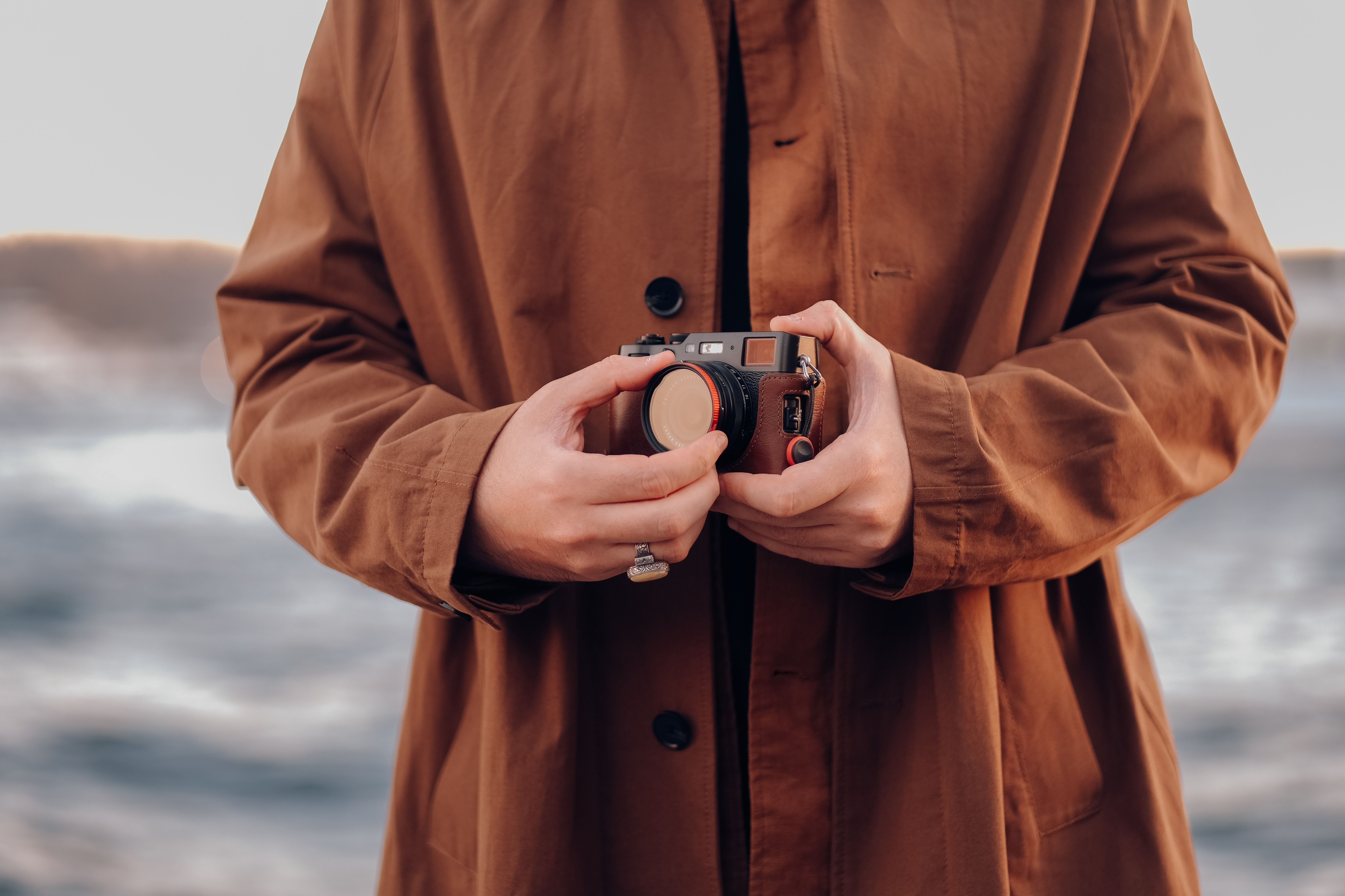 A close-up shot of a person holding a camera wearing a trench coat outdoors.