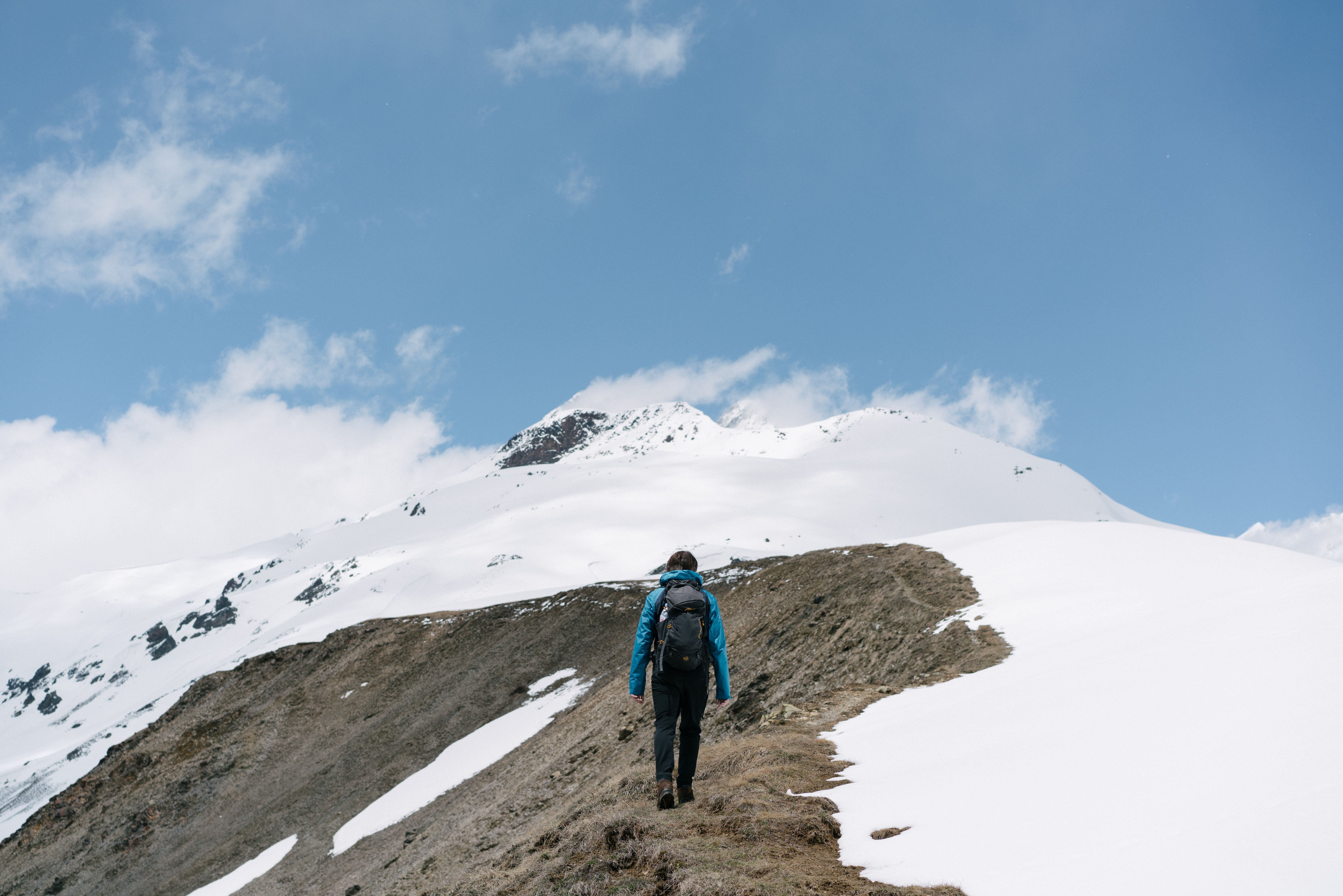 Man hiking in snowy mountains, capturing adventure and wanderlust in a stunning blue-sky setting.