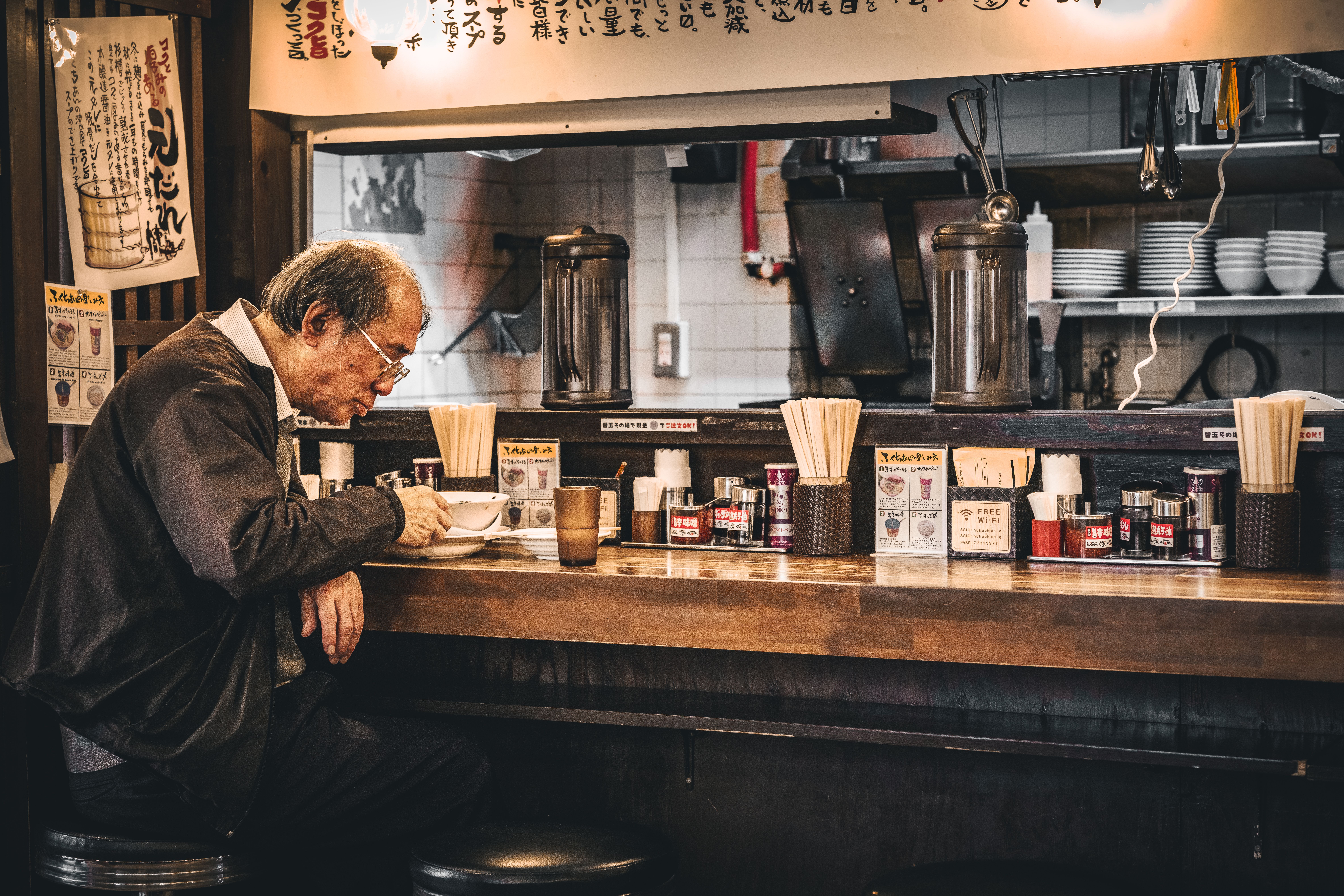 Elderly man dining alone at a traditional Tokyo ramen shop, savoring Japanese cuisine.
