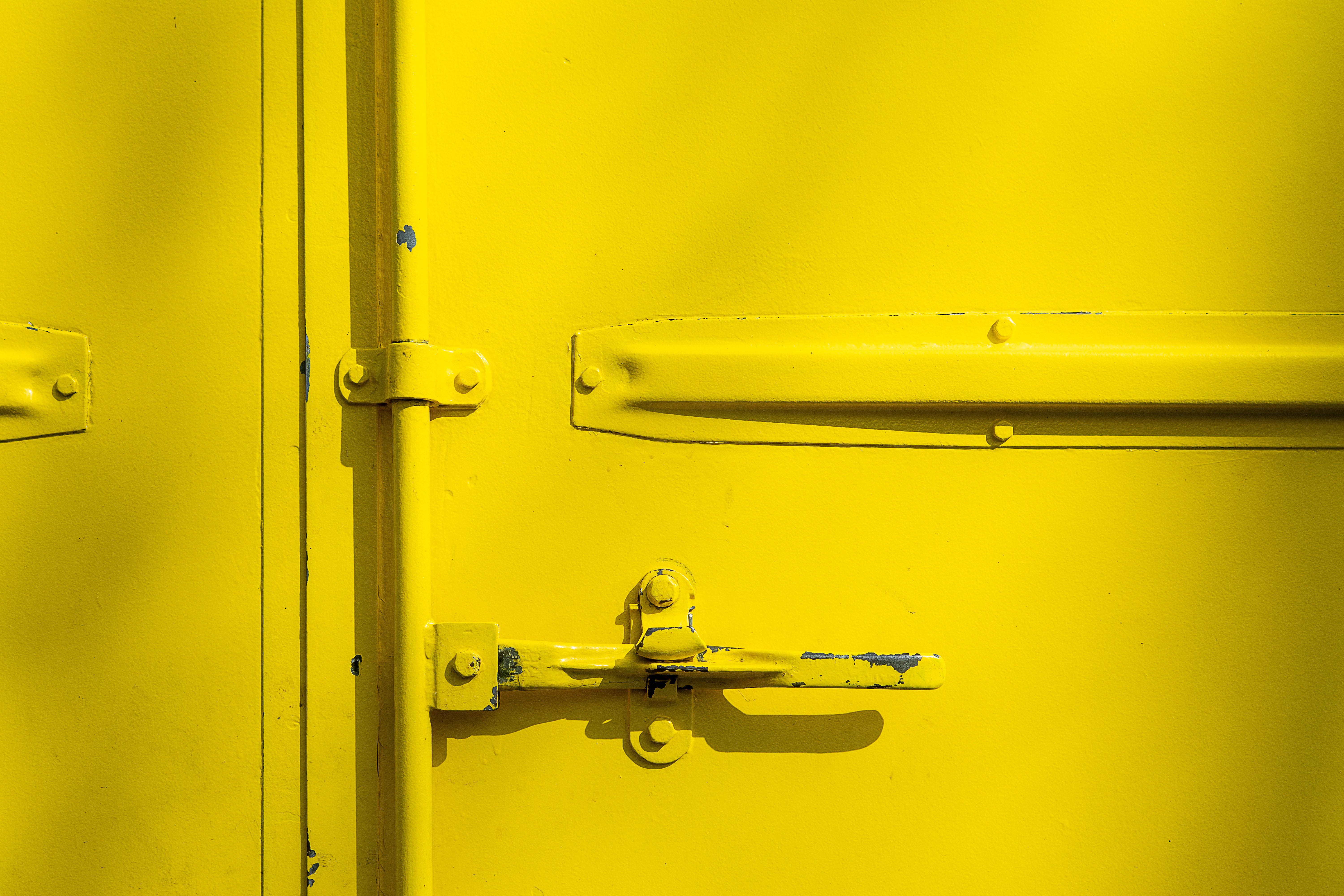Close-up of a yellow metal door with a latch, highlighting industrial design and texture.