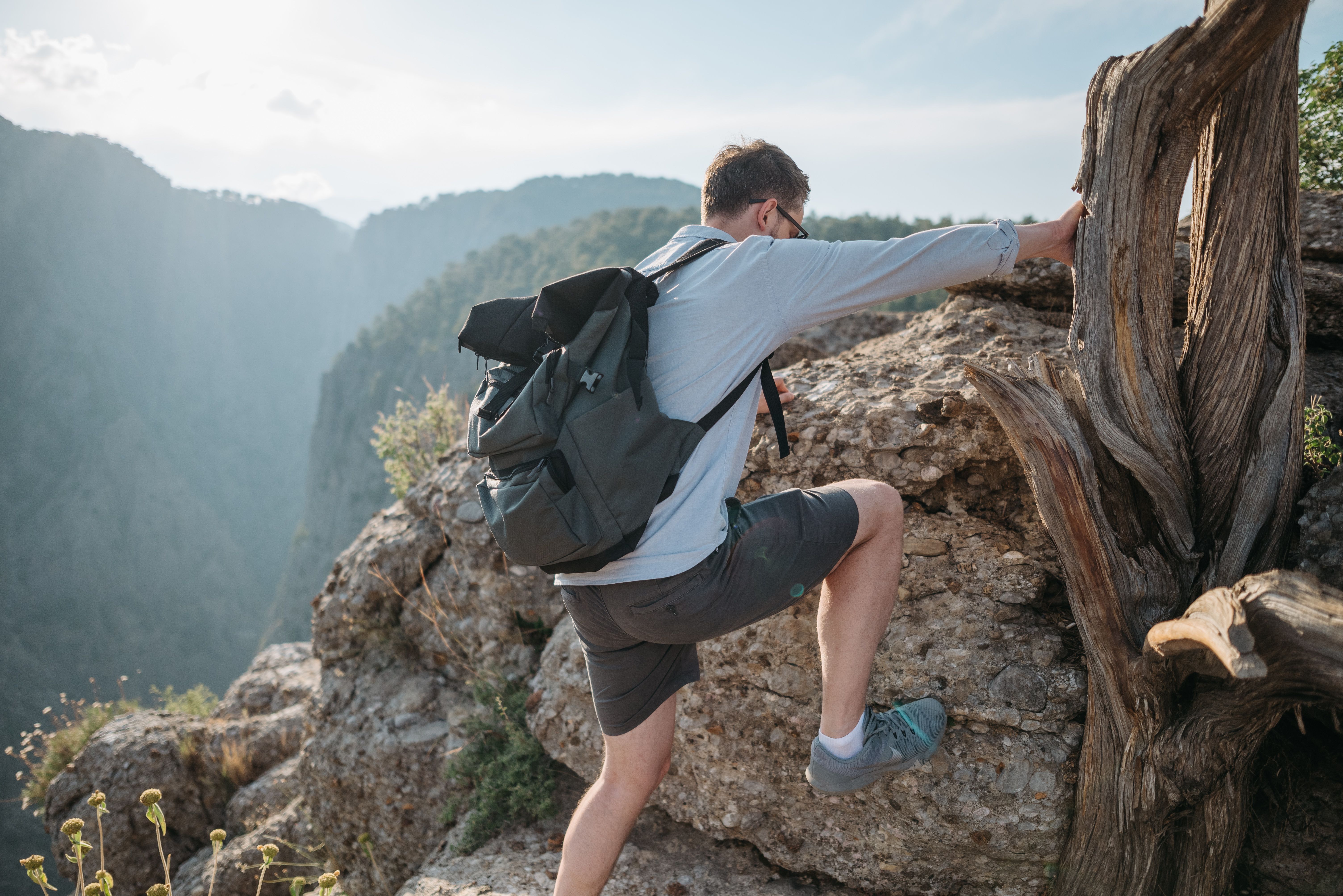 A man climbs rocky terrain with a backpack, showcasing adventure and nature exploration.