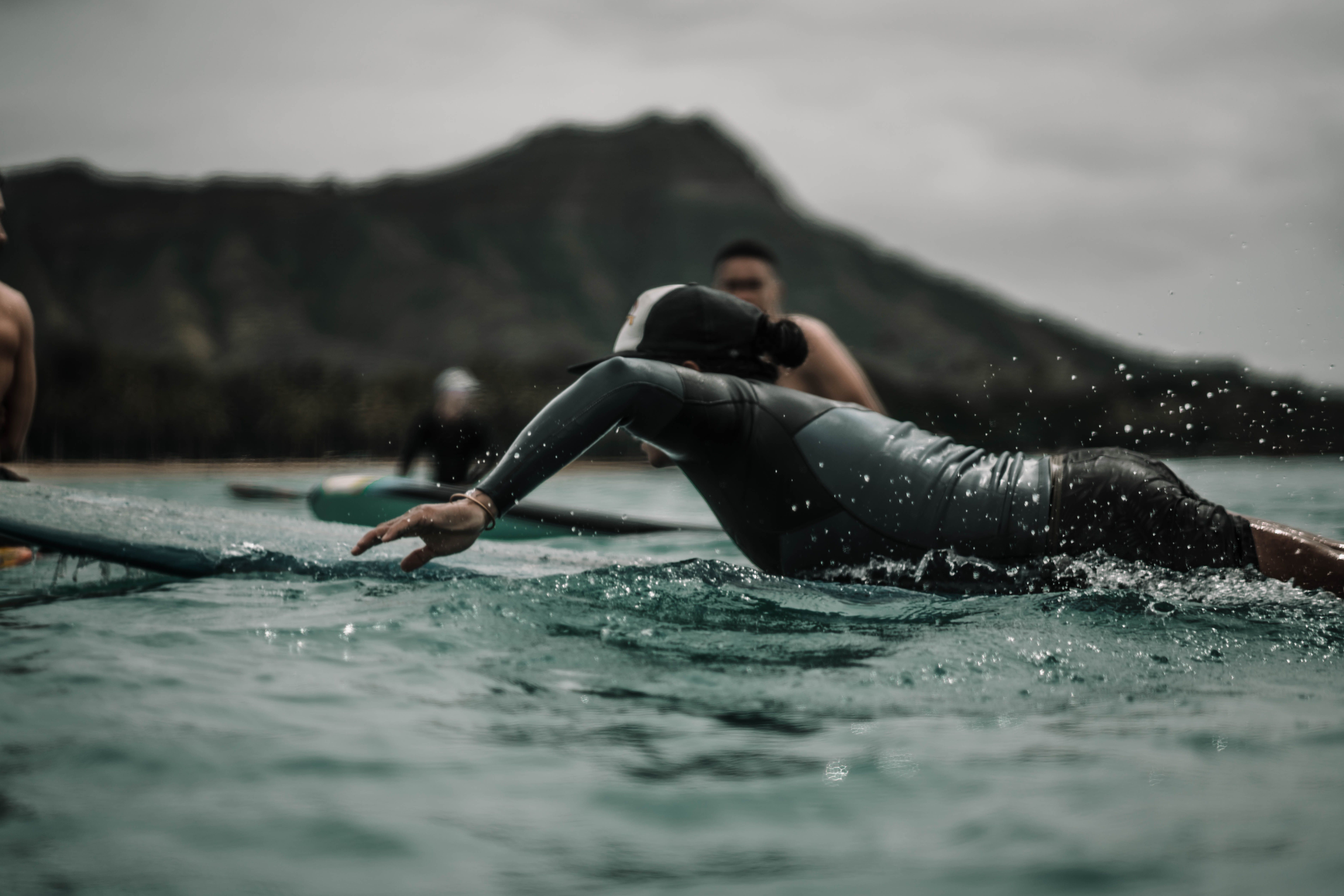 Surfers paddling in the ocean with a mountain view under overcast sky, capturing the essence of adventure.