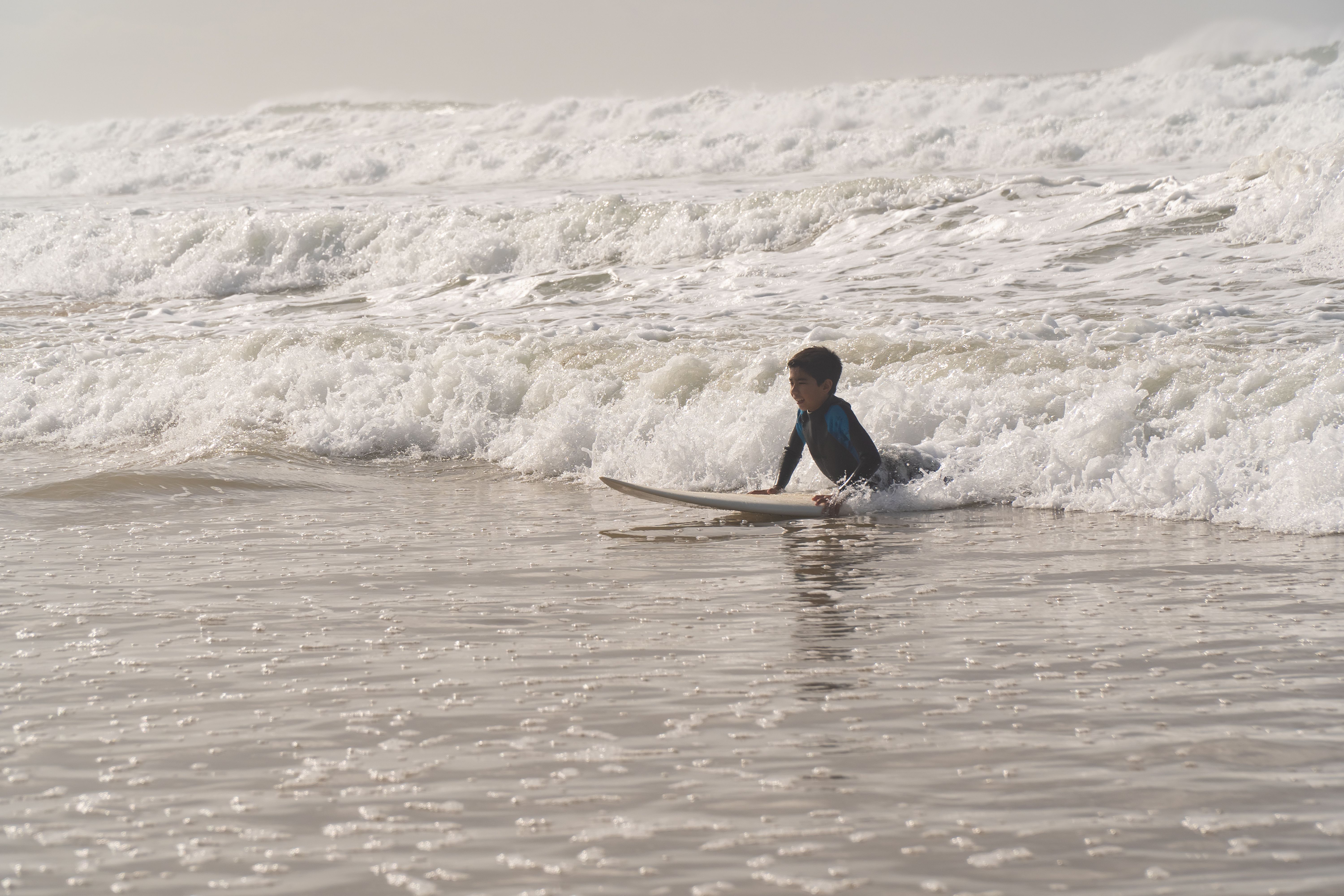 A child learning to surf at a Portuguese beach with waves crashing around him.