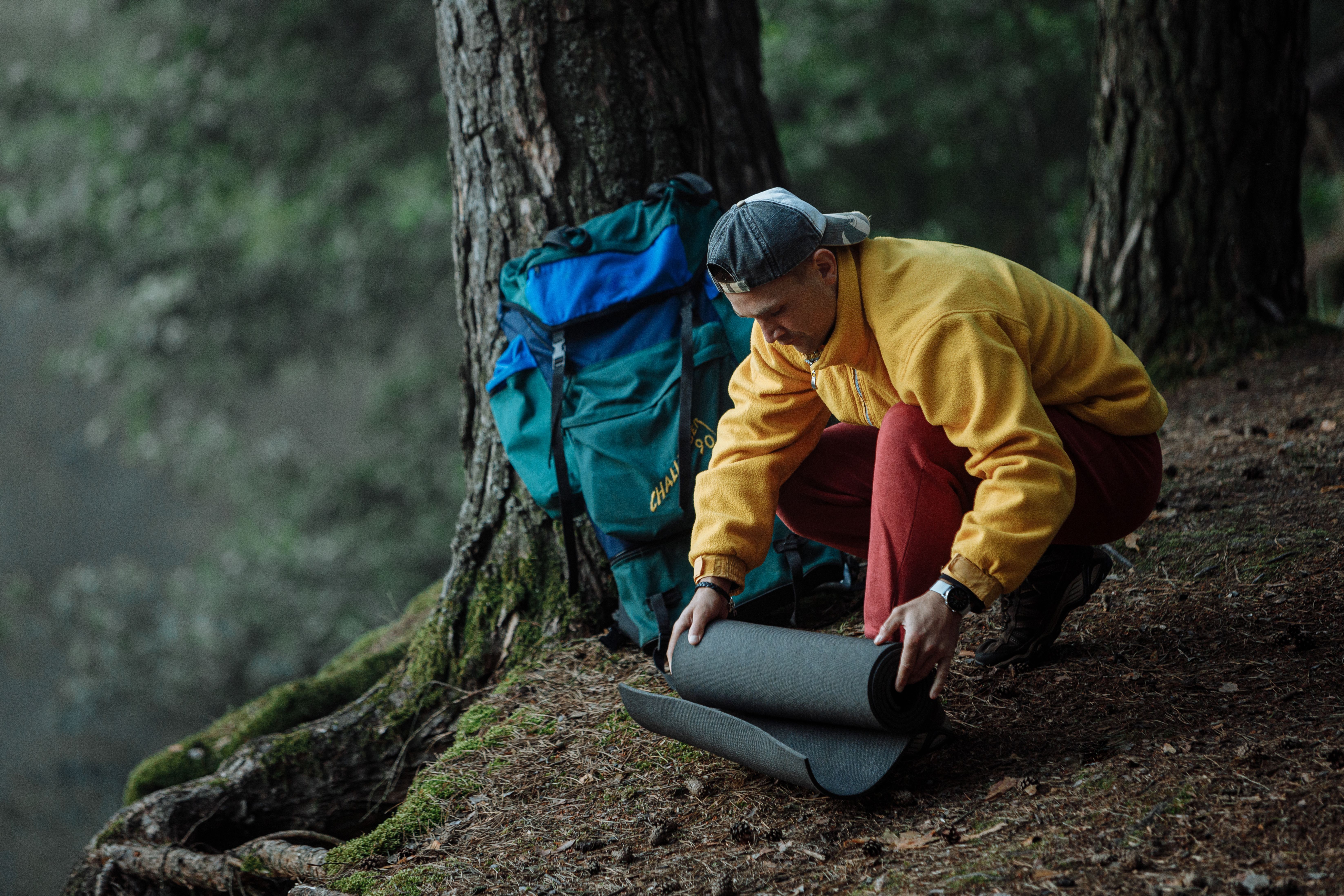 Man sets up camping gear under trees, readying for an outdoor adventure.