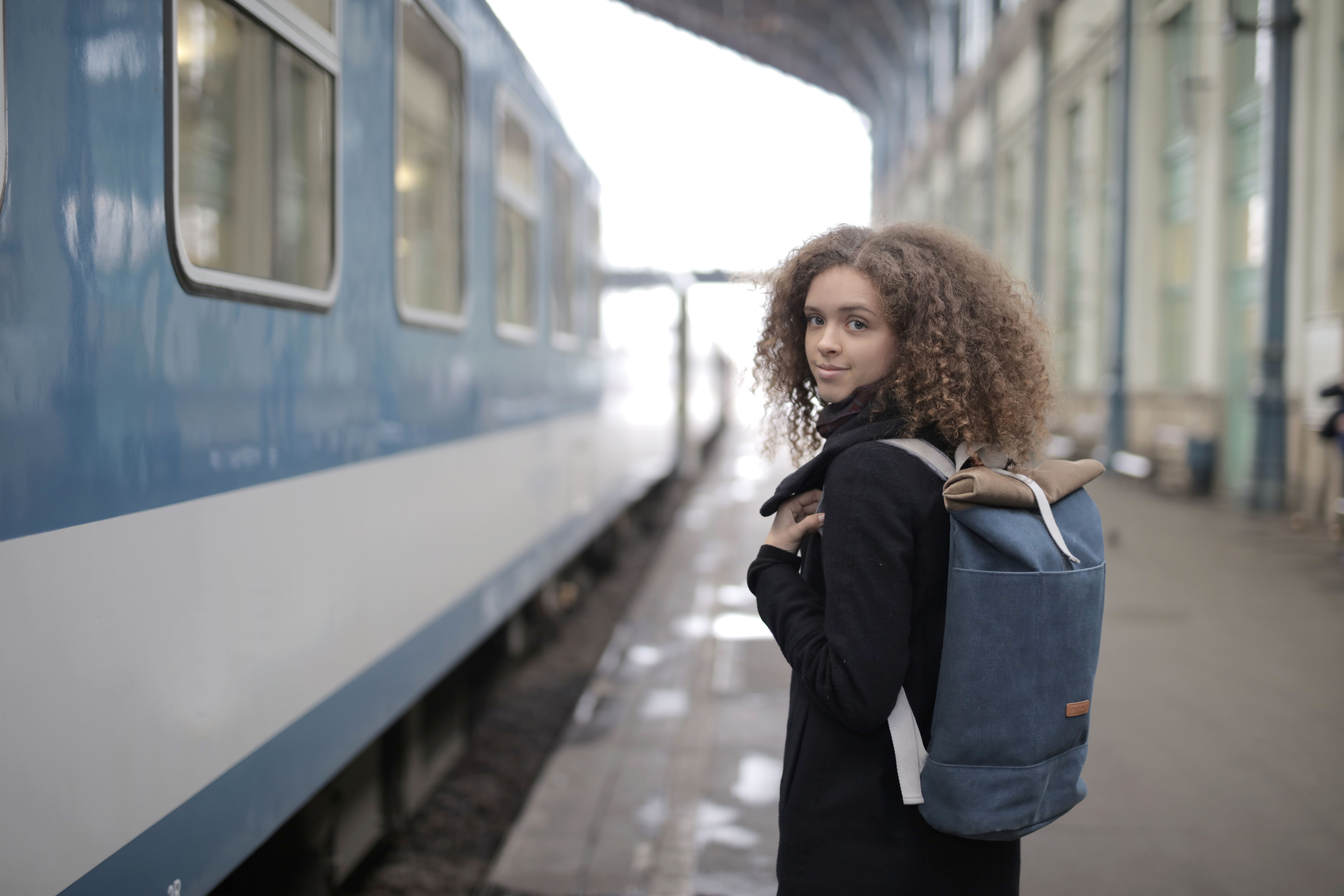 A young woman with a backpack waiting at a train station platform, ready to travel.
