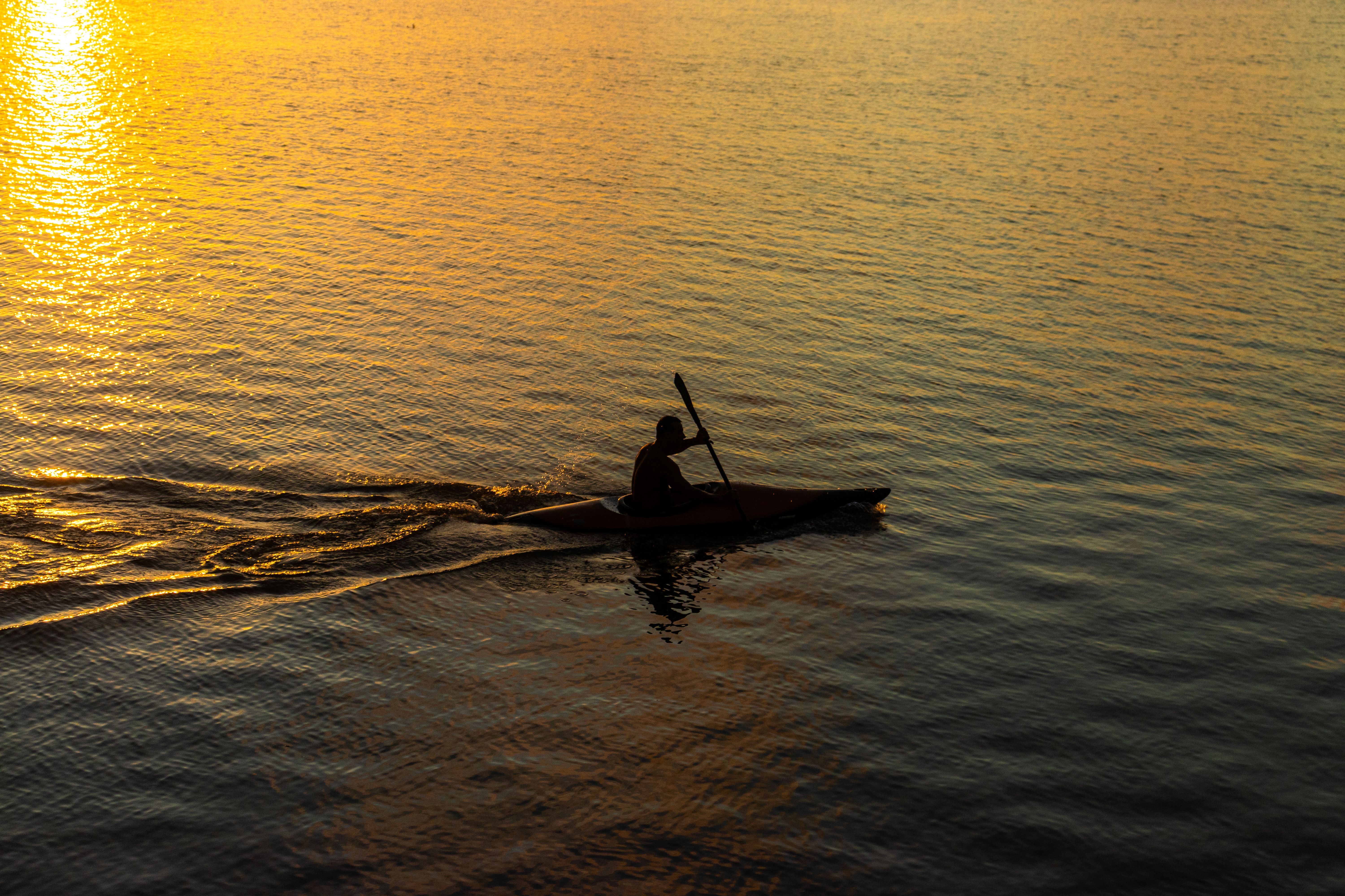A kayaker paddling in silhouette against a stunning sunset on Brazilian waters, creating a tranquil scene.