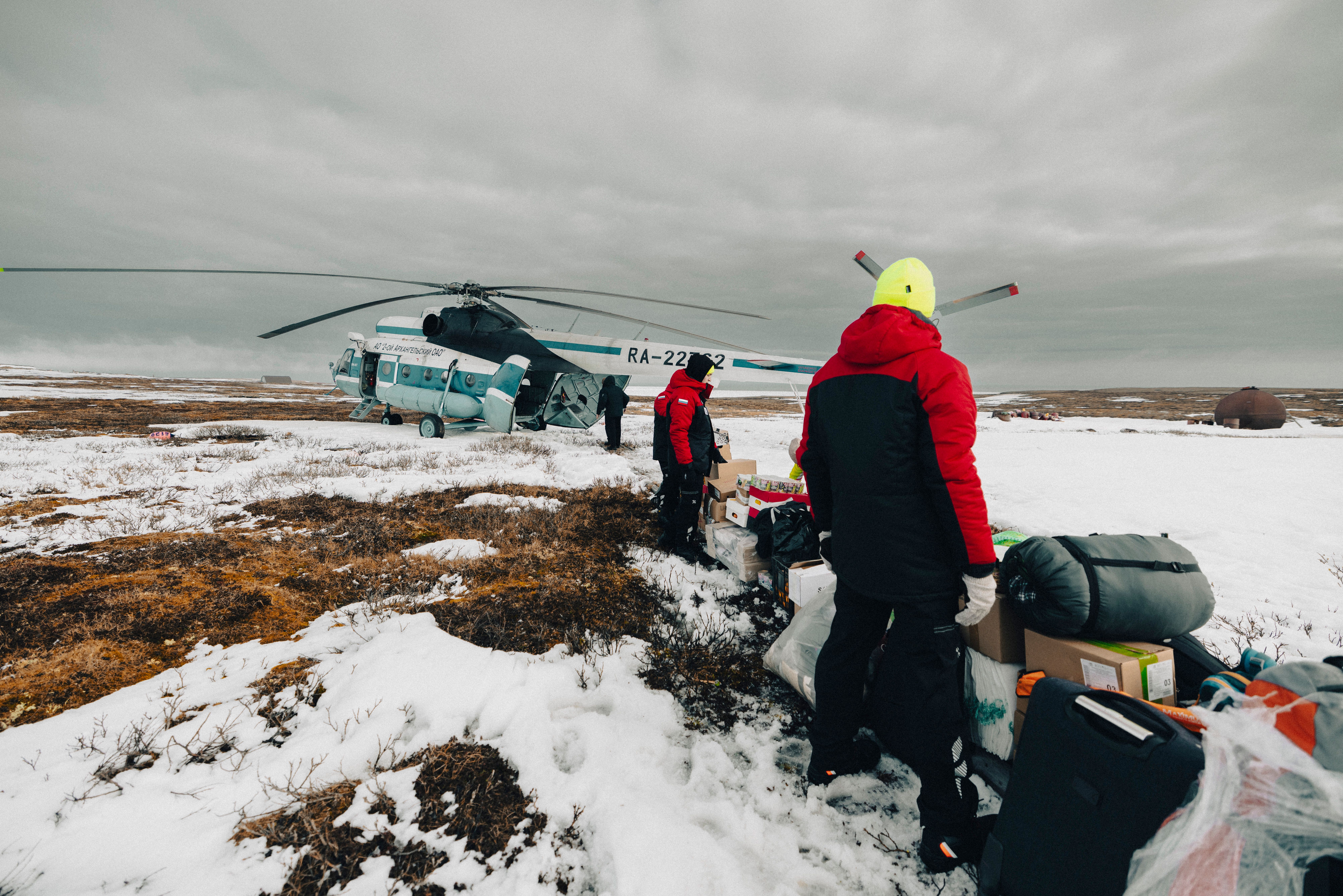 Weatherproofed explorers unloading essentials from helicopter in icy tundra landscape.