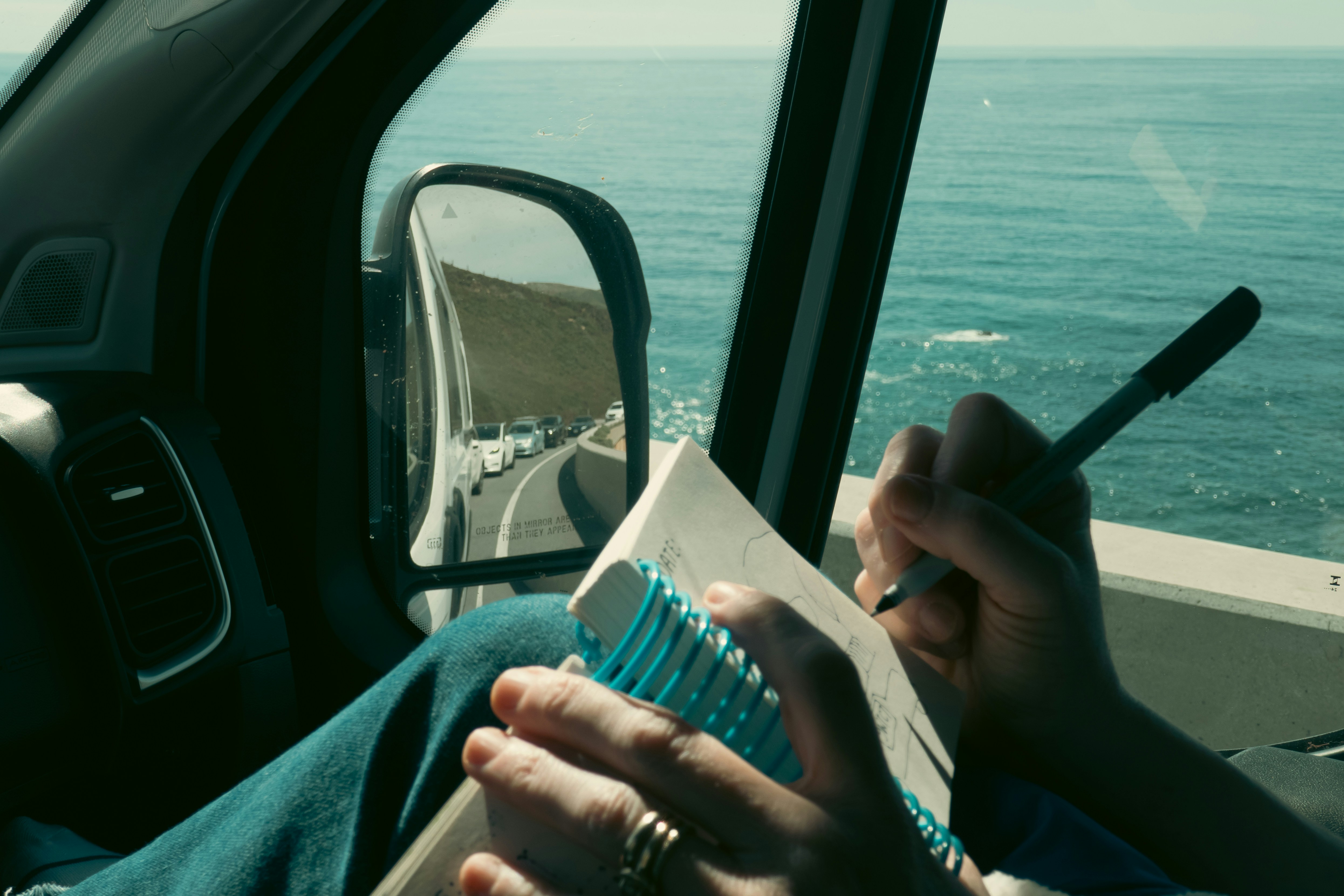 Person writing in a notebook inside a vehicle.