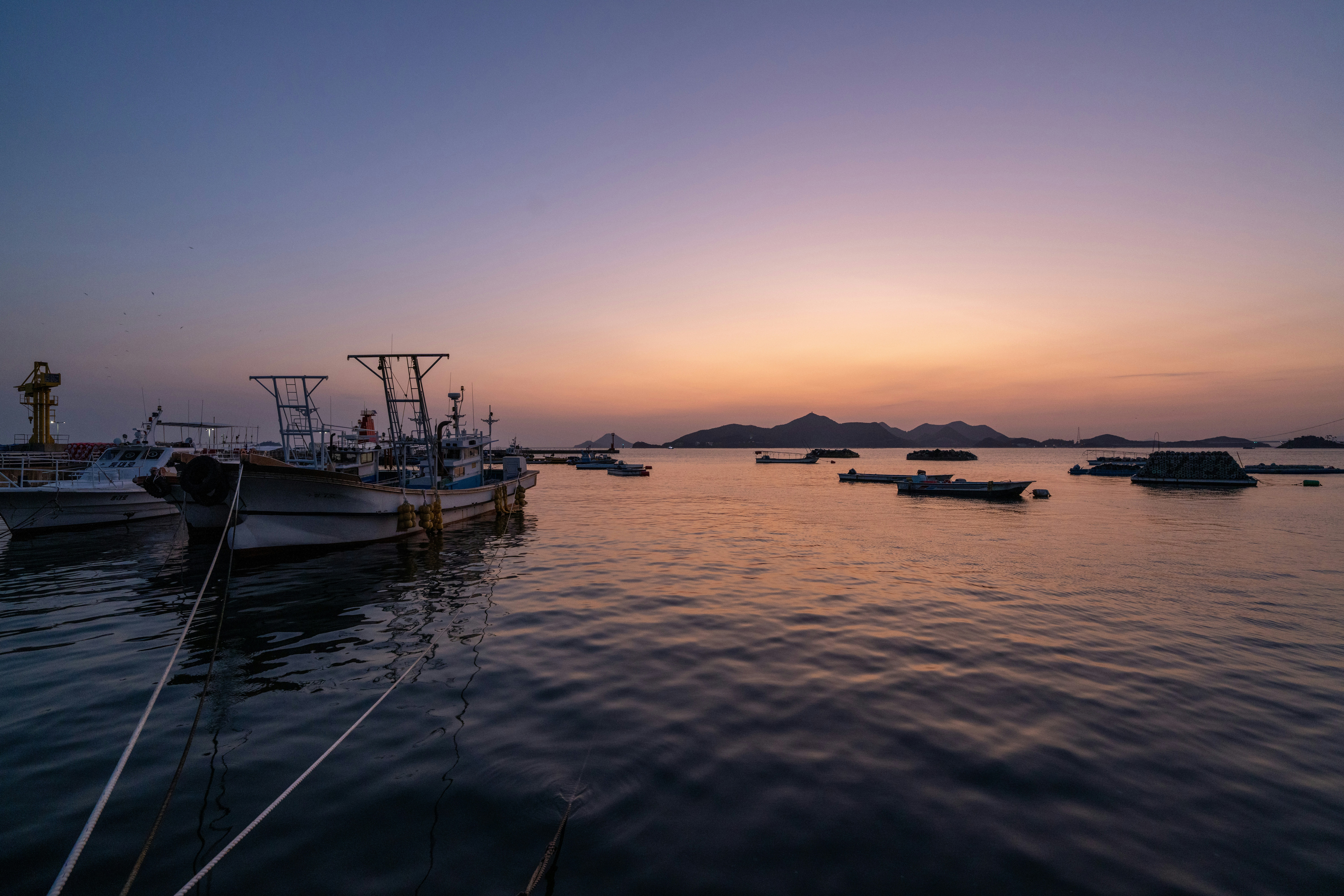 Calm water with boats and a lighthouse at sunset.
