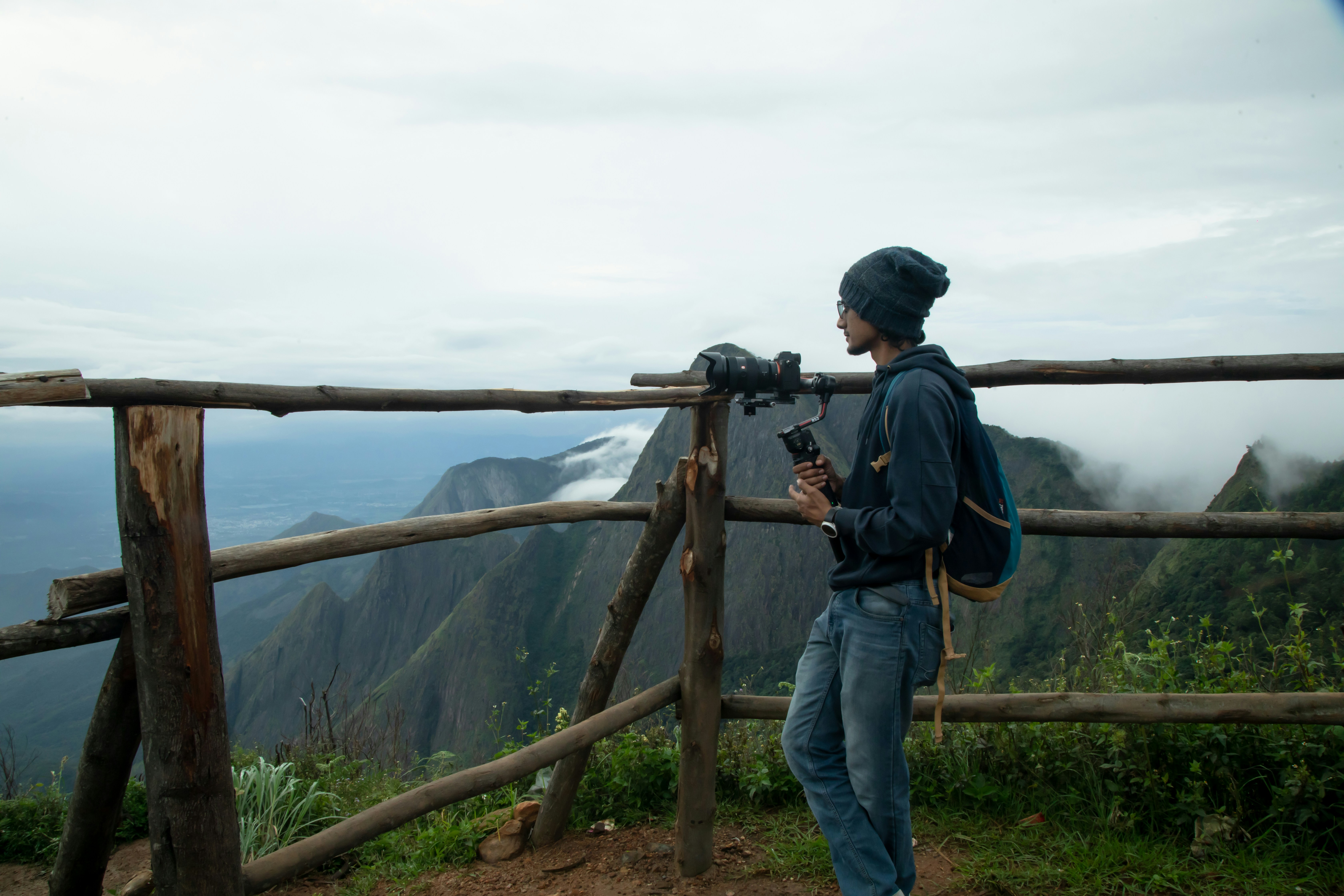 A man standing on top of a mountain next to a wooden fence