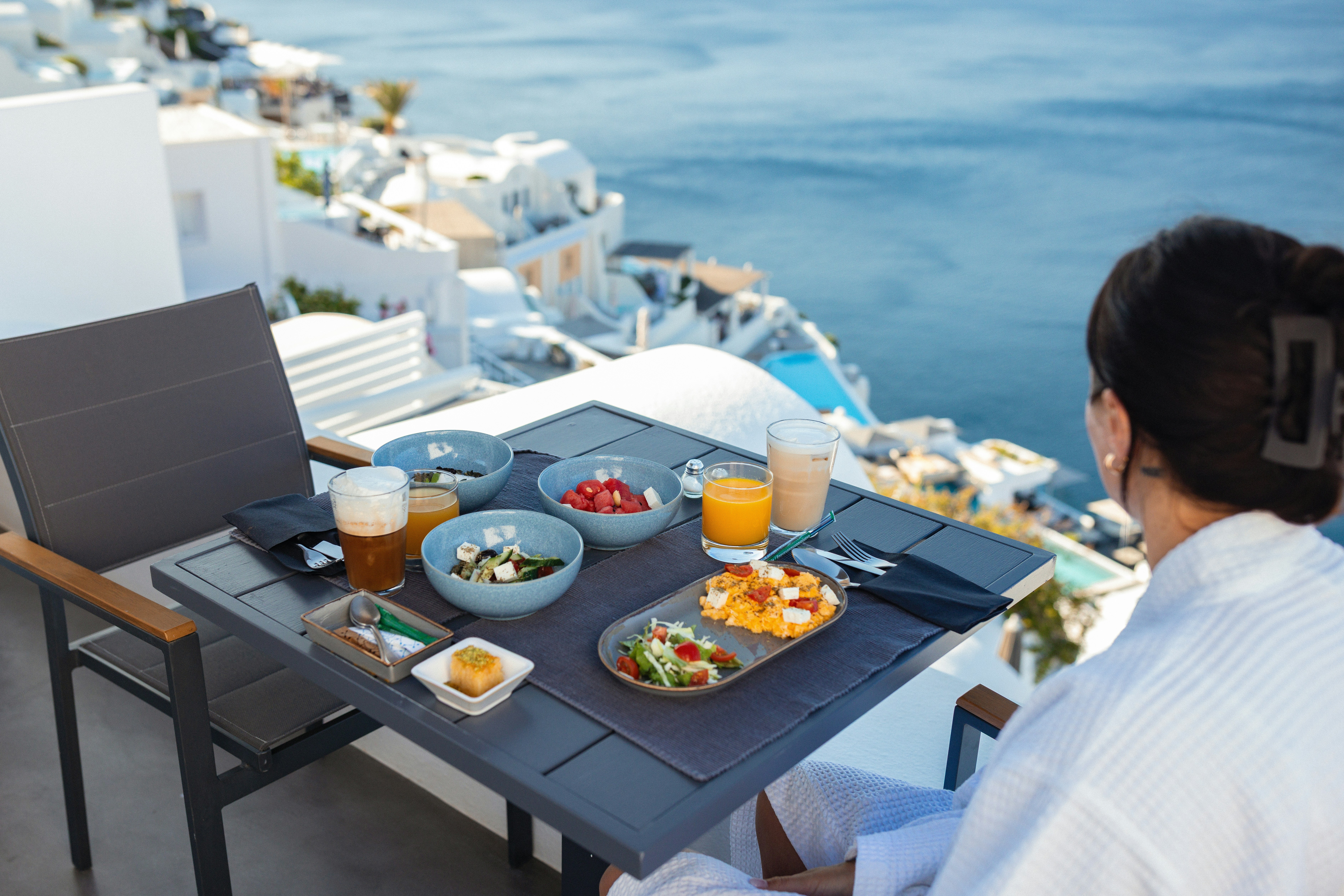 Woman enjoying breakfast on a balcony overlooking the sea.